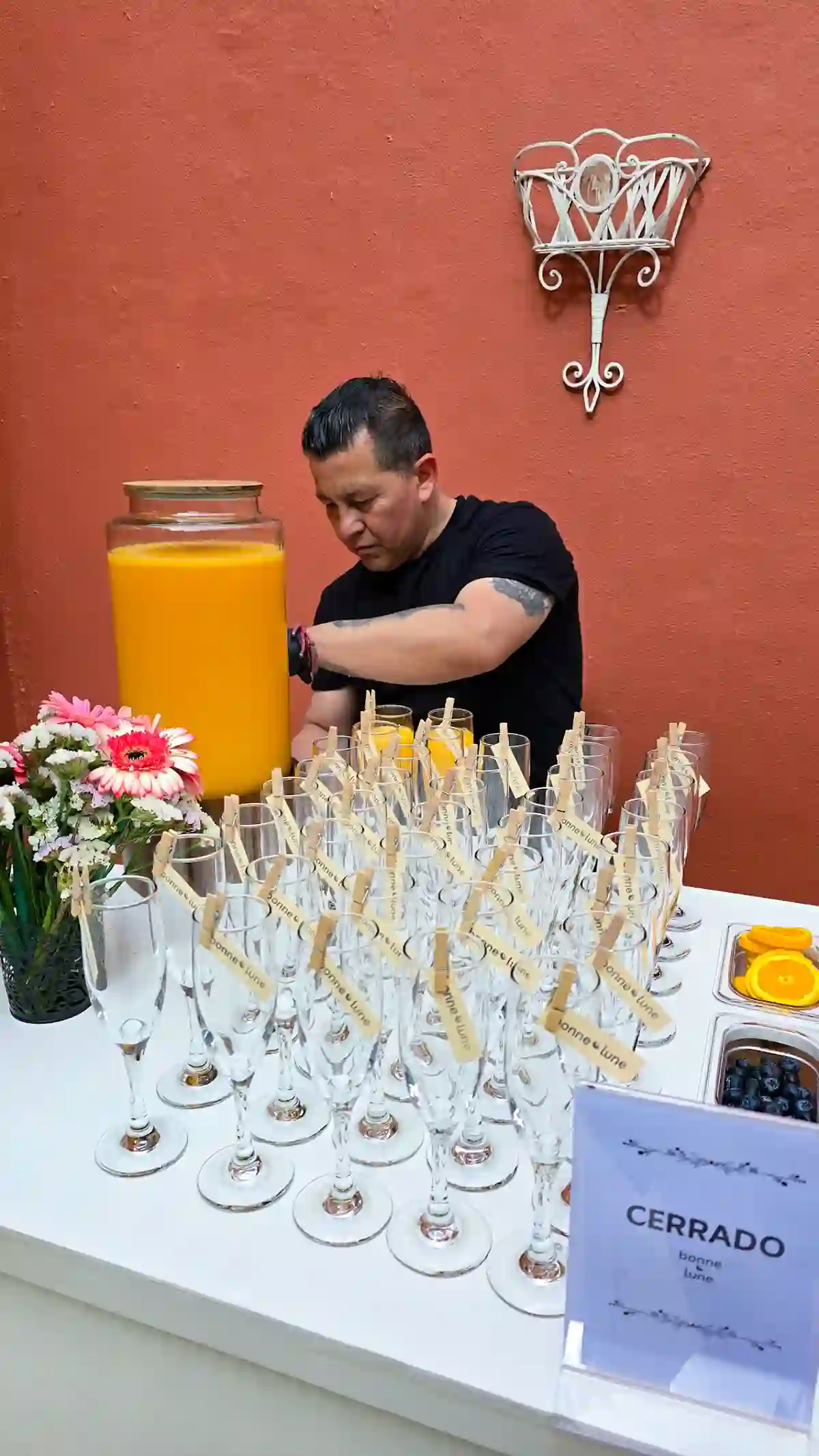 Mesero de Bonne Lune sirviendo jugo de naranja en copas con flores de decoración, barra de mimosas lista para servicio
